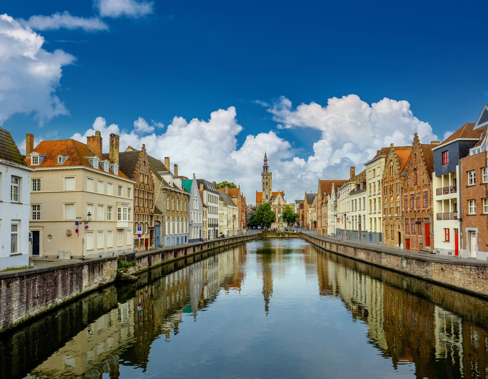 A quiet canal in Bruges lined with historic houses under a blue sky