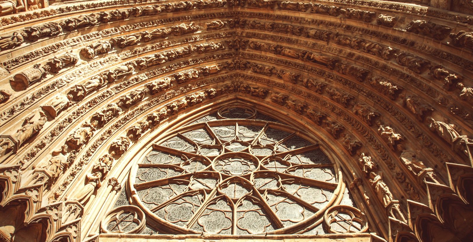 The rose window and carved portal of Reims Cathedral in warm sunlight
