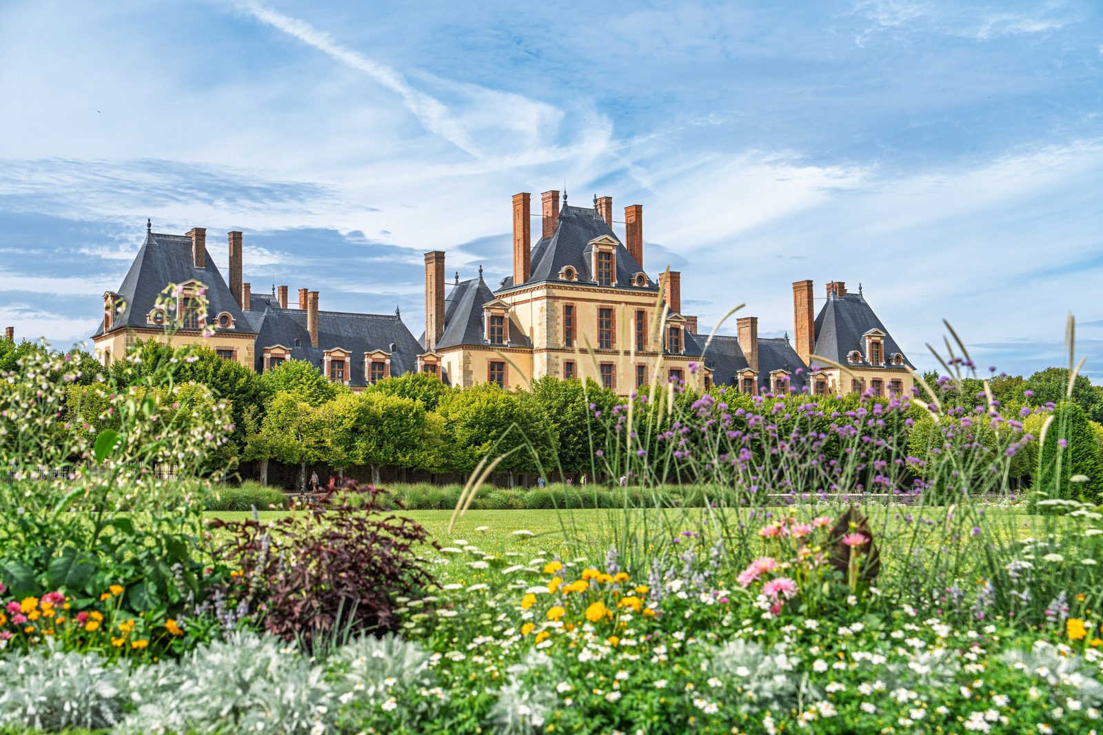 Chateau de Fontainebleau rising above a flower garden with pink, yellow and purple blooms