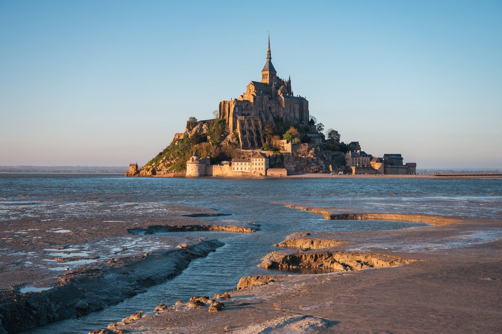 Mont-Saint-Michel at low tide in warm evening light with water channels on the sand
