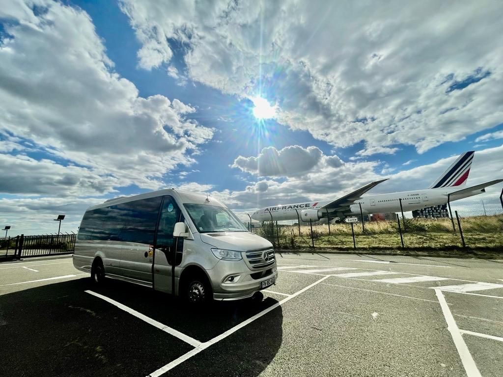 Silver Mercedes Sprinter minibus parked at an airport with an Air France plane behind it
