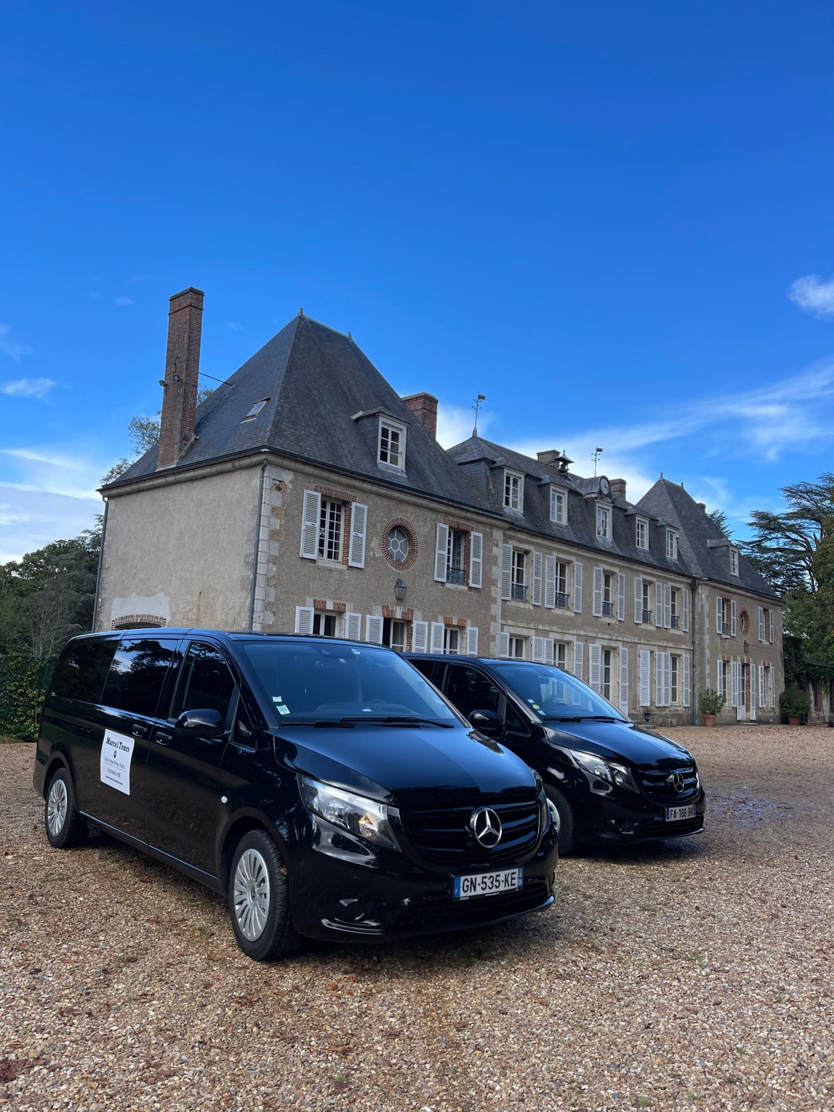 Two black Mercedes Vito vans with a Marcel Tours sign parked in front of a French manor house